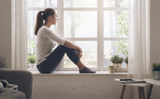 Woman sitting on window ledge - feeling sad about friendship drifting apart. See that friendships ebb and flow. Your best friend might not be exactly who you are over time. Healthy relationships grow together