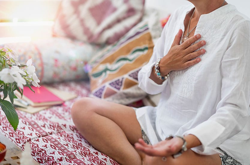 Spiritually aligned woman meditating with hand on heart.