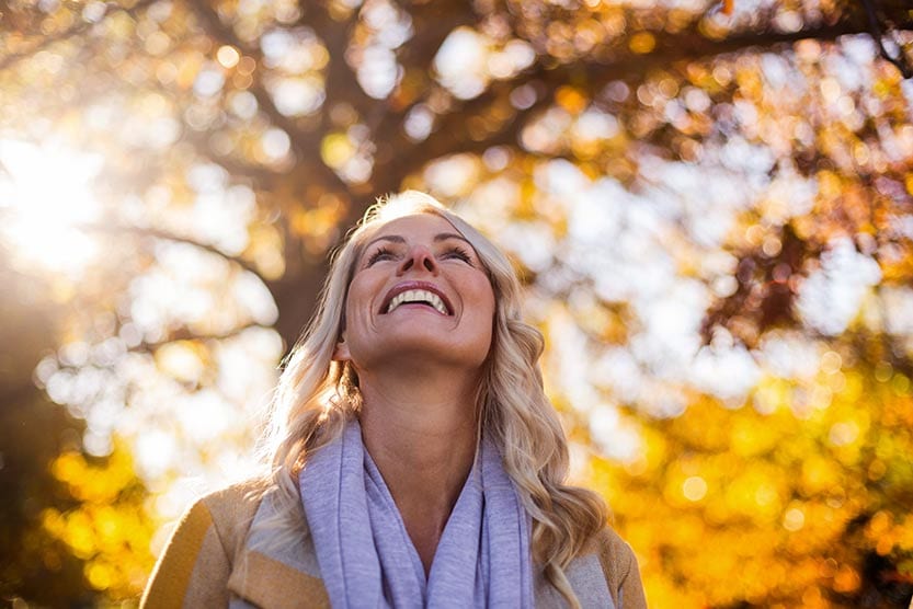 Woman smiling while looking through trees at sunny sky