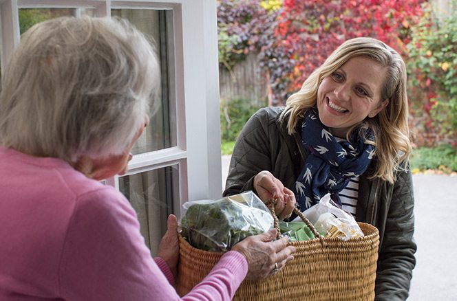 Woman volunteering in her community by delivering food to an elderly neighbor.