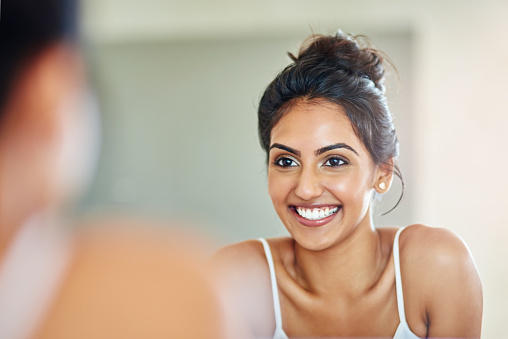 Woman smiling at herself in mirror. Idea of self-kindness.