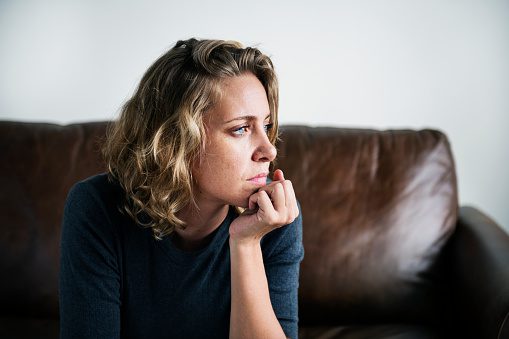Single woman, looking upset while seated on a couch, feeling that it's hard to be a single mom.