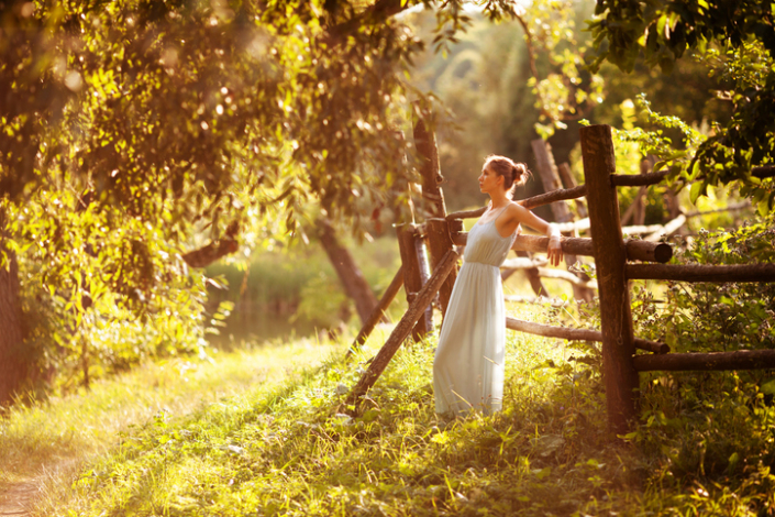 Young woman in a dress is leaning against the hedge in the evening in the garden slow down for calm and clarity